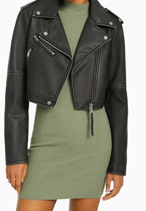 Veste en cuir noire courte avec fermetures éclair argentées portée sur une robe côtelée ajustée vert olive sur une personne.