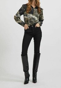 Blus med lång ärm och krage i en texturerad, flerfärgad mönstring. Höga svarta jeans kombinerat med knähöga, glansiga svarta stövlar.