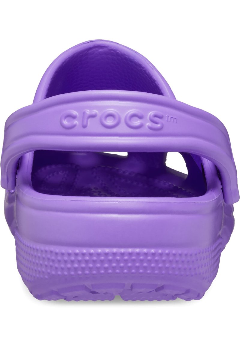 Zuecos de plástico morados con diseño de parte trasera abierta, que cuentan con una plantilla texturizada, una marca prominente y una suela ligeramente elevada y punteada.