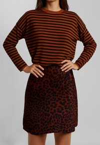 Maglietta a maniche lunghe a strisce marroni e nere abbinata a una gonna a stampa leopardata marrone e nera, con una vestibilità comoda e una texture liscia.