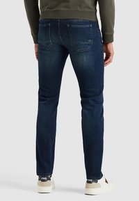 T tumma siniset slim-fit farkut, joissa on hieman haalistunut pinta, viisi taskua ja merkkitikkauksia. Yhdistettynä valkoisiin ja harmaisiin lenkkareihin.