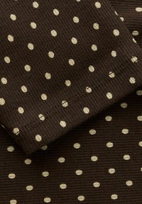 Brunt stoff med kremfargede prikkemønster, ribbet tekstur, med synlige sømdetaljer langs kanten.