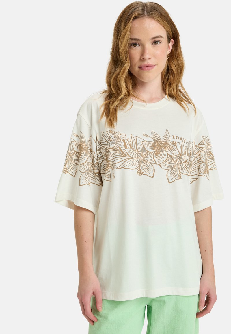 White t-shirt featuring a gold floral design across the chest, short sleeves, and a relaxed fit, paired with light green pants.