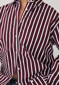 Burgundy and white striped button-up shirt with a collar, featuring a relaxed fit and visible buttons along the front and cuffs.