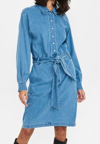Jeansklänning med krage, långa ärmar, knappstängning fram och ett matchande bälte i samma tyg. Plagget är i medelblått och har en mjuk textur.