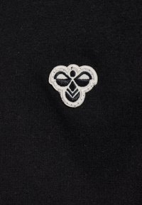 Schwarzer Stoff mit strukturierten Oberflächen, der ein weiß gesticktes Emblem einer stilisierten Biene oder eines Insekts mit markanten Formen und Details zeigt.