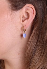 Gouden creolen met een lichtblauwe hartvormige steen, met een gladde textuur en een kleine sluitingaccent. Draagt aan een oor.