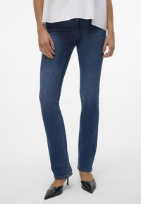Mörkblå denimjeans med en figurnära design, raka ben och subtila sömnadsdetaljer, kombinerade med svarta spetsiga klackar.