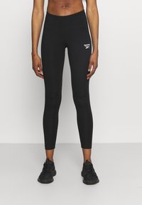 Svarta tights i stretchmaterial, med hög midja och en liten vit logotyp på vänster lår. Slät textur, figurnära design.