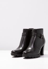 Botines de cuero negro hasta el tobillo con punta redonda, cremallera lateral, correa ajustable con hebilla y un tacón grueso y texturizado.