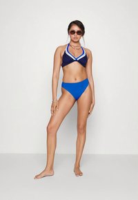 Conjunto de bikini com top halter azul-marinho com detalhes em branco e cuecas de cintura alta em azul vibrante. O material parece elegante e suave.