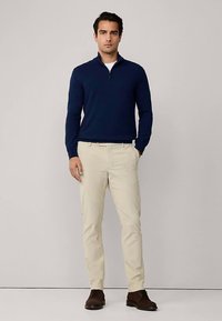 Granatowy sweter na zamek z lekkiego dzianego materiału, zestawiony z jasnobeżowymi chinosami i brązowymi butami. Strój ma swobodny, a zarazem elegancki wygląd.