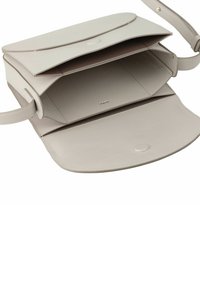 Bolso de mano de cuero beige con cierre de solapa, que cuenta con dos compartimentos principales, forro interior mínimo y un sutil detalle del logo en oro.