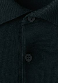 Krupni plan crnog pletenog tkanja s dva crna gumba i preklopljenim ovratnikom na odjevnom predmetu.