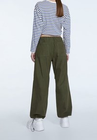 Pantaloni cargo verdi con due tasche posteriori, abbinati a una camicia a righe navy e bianca, a maniche lunghe e cropped, e sneaker bianche spesse.