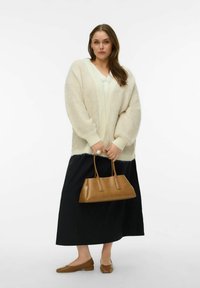 Krēmkrāsas adīts kardigans ar dziļu V-veida izgriezumu, kopā ar melnu garu svārku un brūnām plakanām kurpēm. Tur brūnas ādas rokassomu.