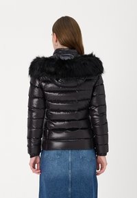 Black padded jacket with a glossy finish, featuring a removable black fur hood, elastic cuffs, and stitched horizontal panels.