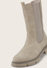 Beige Wildleder-Stiefelette mit elastischen Seitenpaneelen, runder Zehenform, strukturierter Oberfläche und robuster Gummisohle, die für Langlebigkeit und Komfort ausgelegt ist.