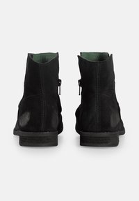 Bottes chelsea en daim noir avec un petit talon, dotées d'une fermeture éclair sur le côté, d'une texture lisse et d'une doublure verte visible sur le dessus.