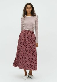 Jupe longue bordeaux avec un motif abstrait, taille élastique. Associée avec un haut ajusté à rayures à manches longues en blanc et bordeaux. Chaussures blanches à enfiler.
