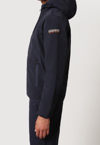 Giacca con cappuccio blu navy realizzata in materiale resistente, dotata di tasca con zip e dettagli del logo ricamato sulla manica.