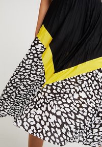 Vestito nero con top plissettato, accento diagonale giallo e gonna a stampa leopardata nero e bianco. Tessuto liscio, design di lunghezza media.