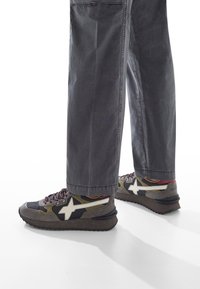 Ben klädda i grå byxor och flerfärgade sneakers med vit stjärndesign och mörka fläckiga sula, mot en vit bakgrund.