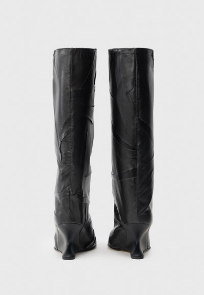 Melnas ādas zābaki līdz ceļam ar gludu tekstūru un leņķveida šuvēm. Piemēroti ar veidotu papēdi, kas izceļ unikālu dizainu.