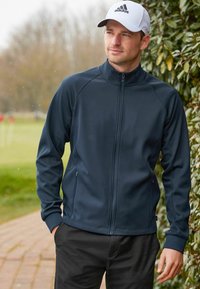 Chaqueta deportiva de color navy con cremallera frontal completa, cuello alto y puños elásticos. Cuenta con paneles laterales texturizados y bolsillos con cremallera.