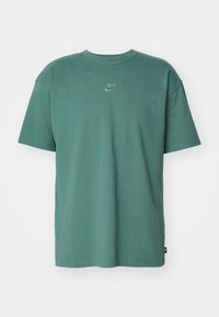 Zielona bawełniana koszulka z okrągłym dekoltem, krótkimi rękawami i subtelnym, haftowanym logo Nike na piersi. Gładka faktura i luźny krój.