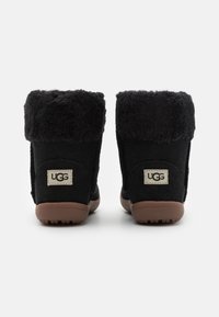 Bottines noires en daim avec un col en peau de mouton noir pelucheux, dotées d'une semelle en caoutchouc et d'un petit patch logo à l'arrière.