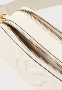 Bolsa de pele creme com dois compartimentos com fecho dourado. O exterior texturizado inclui detalhes em relevo e um accentuado cosido.