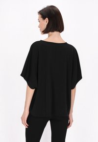 Top negru, cu croială lejeră, cu mâneci tip batwing, textură moale și decolteu rotund, asortat cu pantaloni negri. Vedere din spate.