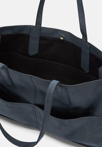 Niebieska zamszowa torba typu tote z dwoma długimi uchwytami, posiadająca czarne wnętrze i magnetyczne zapięcie. Zawiera wiele wewnętrznych kieszeni.