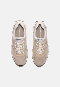 Sneaker sportive beige con tomaia in suede, lacci bianchi e accenti grigi. Presentano una soletta imbottita e una suola in gomma nera testurizzata.