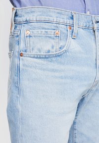 Světle modré džíny z denimu s úzkým střihem, pěti kapsami, měděnými nýty a viditelnými švy. Texturovaná tkanina vykazuje mírné opotřebení.