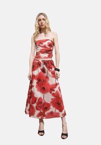 Strapless dress in lightweight fabric features a fitted bodice and flowing skirt, adorned with a red poppy floral pattern on a light background.