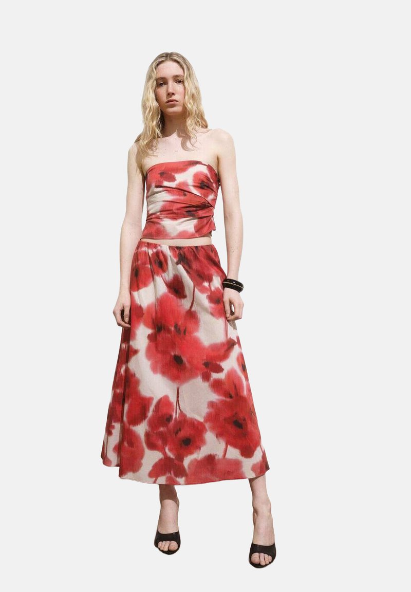 Strapless dress in lightweight fabric features a fitted bodice and flowing skirt, adorned with a red poppy floral pattern on a light background.