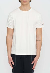 T-shirt en coton blanc à manches courtes, col rond, et avec un petit logo sur la manche gauche. Texture lisse, coupe décontractée.