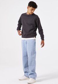 Sudadera gris con cuello redondo, ajuste relajado y puños acanalados, combinada con pantalones vaqueros de pierna ancha en azul claro y zapatillas blancas.