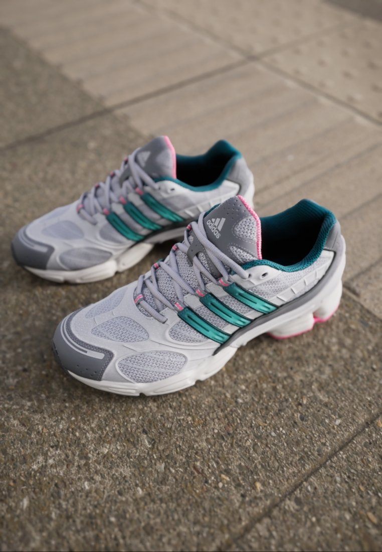 Grijze sportschoenen van mesh en synthetische materialen, met turquoise en roze accenten, een ronde neus en een gestructureerde zool.