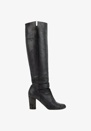 Botte en cuir noire jusqu'au genou avec talon bloc et détail de couture près de la cheville, vue de profil sur fond blanc.