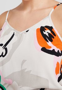 Camisole en satin avec un col en V, présentant des motifs abstraits en orange, rose, noir et vert sur un fond gris clair.