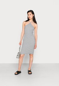 Vestido cinza de jersey com decote halter, silhueta ajustada e comprimento até ao joelho. Usado com sandálias pretas e uma bolsa com padrão de zebra.