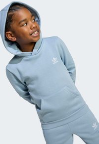 Svijetloplavi pamučni dukserica s prednjim džepom i kapuljačom sa vezicama, sa bijelim Adidas logotipom na prsima i odgovarajućim trenirkom.