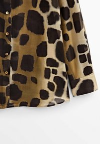 Koszula w panterkę z dużymi czarnymi i beżowymi łatami, wykonana z lekkiego materiału, z zapinaniem na guziki z przodu i klasycznymi mankietami.