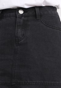 Svart denimkjol med hög midja, prydd med en silverknapp, två framfickor och en slät textur. Klassisk, minimalistisch design.