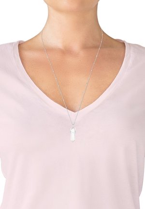 Collana in argento con pendente di cristallo trasparente, esposta su una maglietta rosa chiaro a scollo a V. Design semplice con una leggera lucentezza.