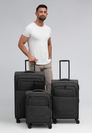 Trois valises en tissu gris de tailles variées, présentant une surface texturée, des poignées rétractables et des roues multidirectionnelles.