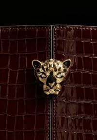 Geantă din piele burgundă cu textură de crocodil, având un închizător în formă de cap de leopard aurit, decorat cu cristale negre și transparente în centru.
